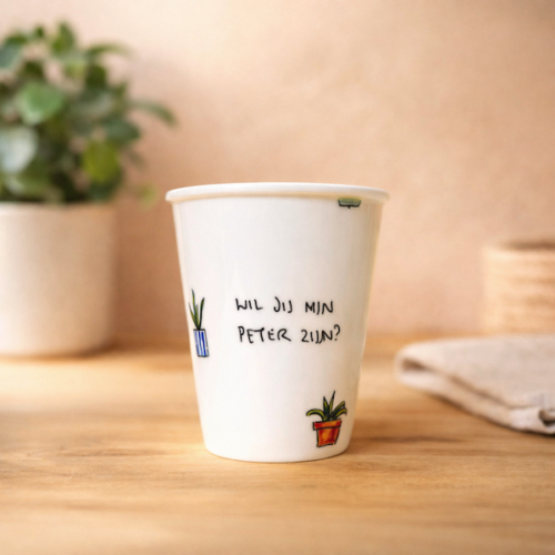 Een porseleinen beker met de tekst 'wil jij mijn peter zijn?' en plantjes eromheen getekend in een gezellige omgeving